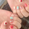 A close-up shot of a hand displaying various cute cartoon press-on nails with pink, green, and red accents.