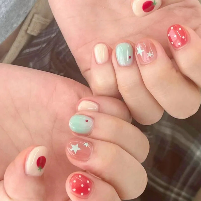 A close-up shot of a hand displaying various cute cartoon press-on nails with pink, green, and red accents.