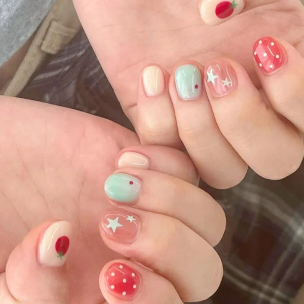 A close-up shot of a hand displaying various cute cartoon press-on nails with pink, green, and red accents.