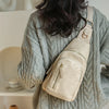 A beige PU leather crossbody sling bag is shown being held by a person wearing a gray knitted sweater.