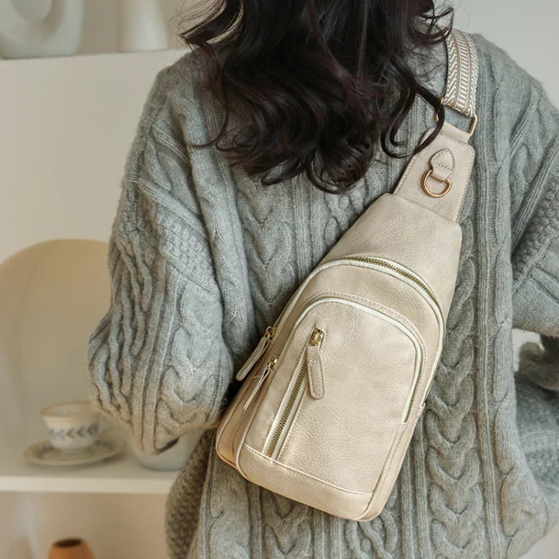 A beige PU leather crossbody sling bag is shown being held by a person wearing a gray knitted sweater.