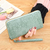 Cartera de tarjeta de cuero PU floral en verde menta grabada junto a una mano y un periódico sobre una superficie de madera.