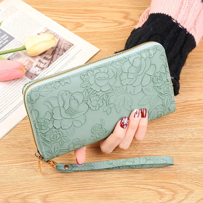Cartera de tarjeta de cuero PU floral en verde menta grabada junto a una mano y un periódico sobre una superficie de madera.