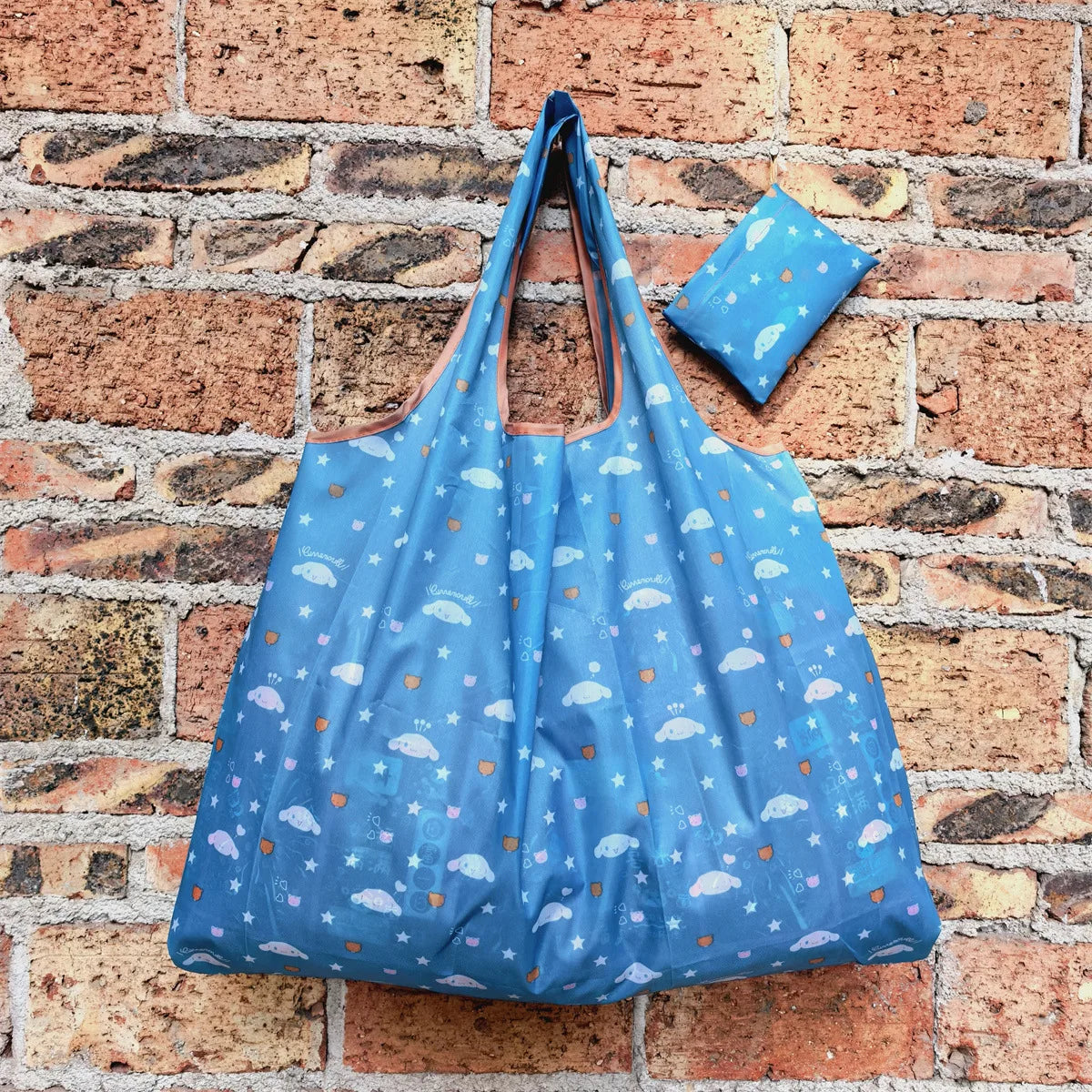 A bright blue reusable shopping bag with a patterned fabric is displayed against a brick wall.