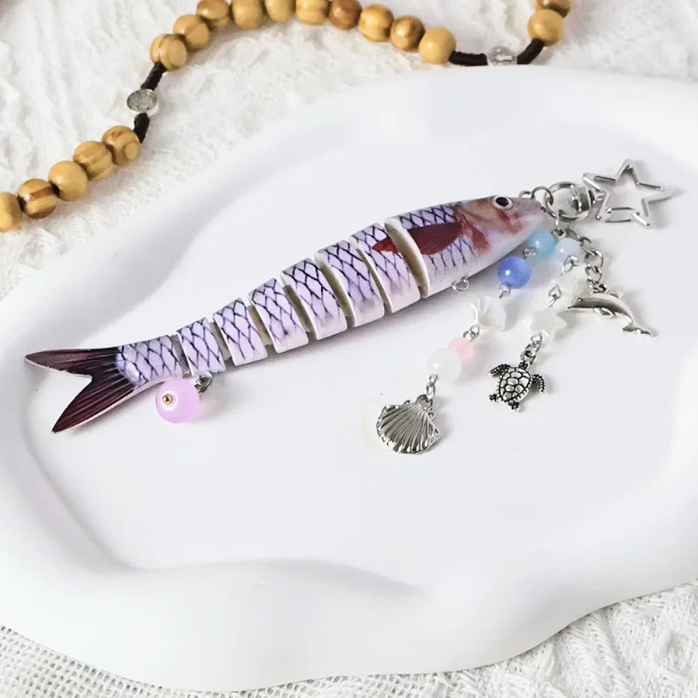 A purple and white simulation fish keychain with dangling charms rests on a white plate.