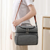 A person is holding a gray insulated double-layer lunch bag with a brown strap.