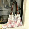 A pink and white patchwork floral shoulder bag with brown leather straps displayed in front of a window.