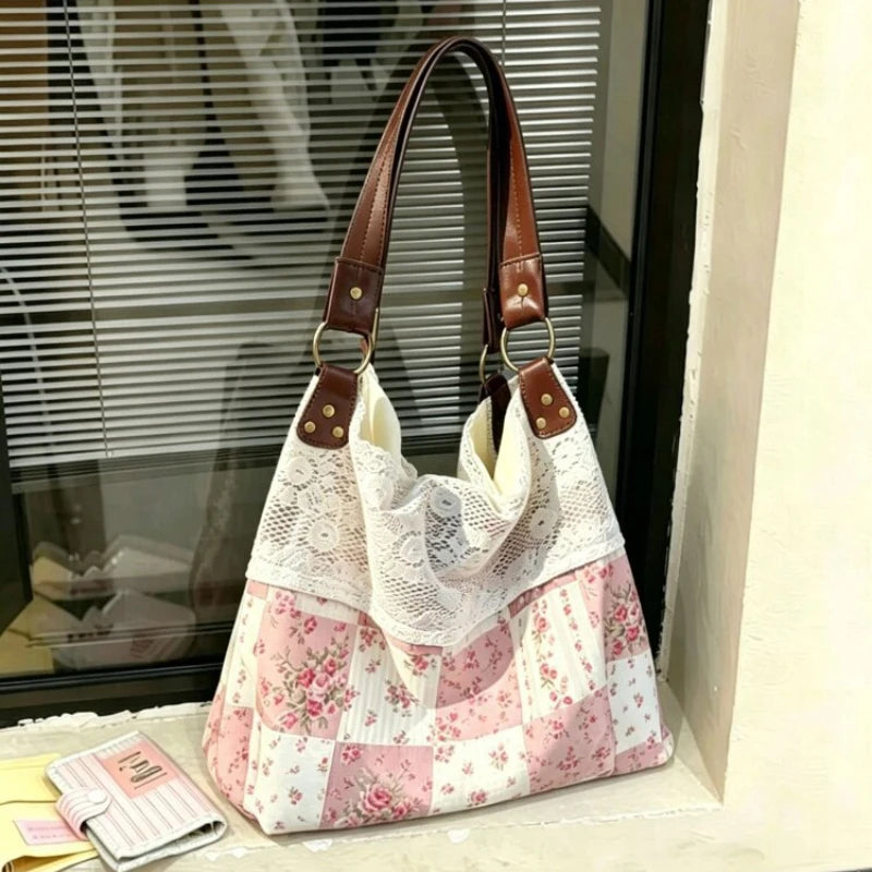 A pink and white patchwork floral shoulder bag with brown leather straps displayed in front of a window.