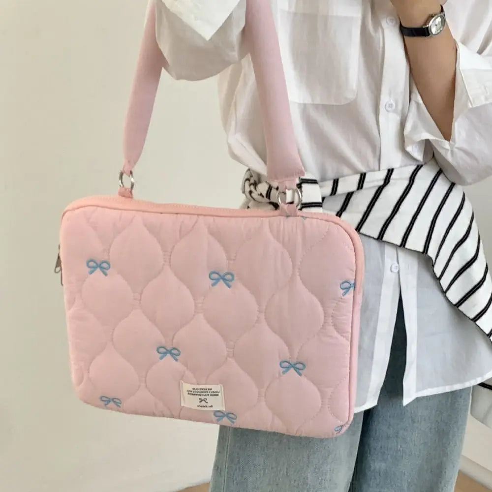 Bolso de portátil acolchado rosa con lazo azul claro, sostenido por una persona con camisa blanca a rayas
