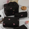 A collection of black quilted cosmetic bags with pink bows and gold hardware displayed on a white surface.