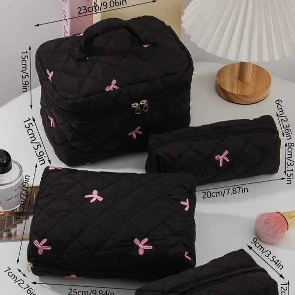A collection of black quilted cosmetic bags with pink bows and gold hardware displayed on a white surface.