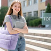A young woman smiling while holding a purple quilted puffer tote bag for school.