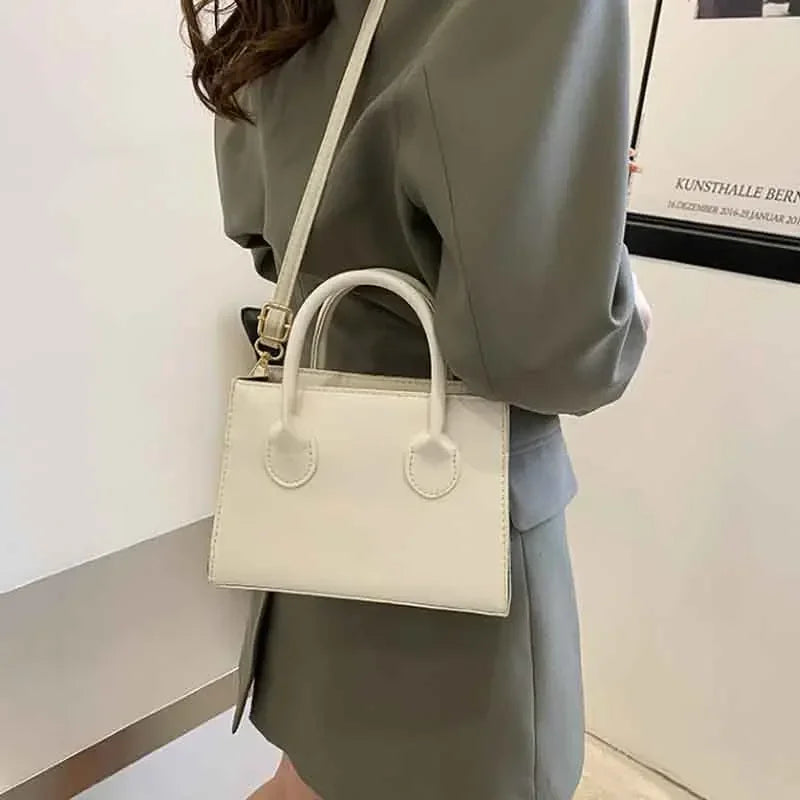 Sac à main en cuir PU beige clair minimaliste avec poignée supérieure, porté par une personne vêtue d'un blazer gris.