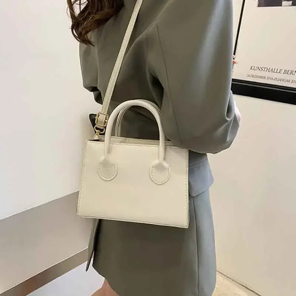Sac à main en cuir PU beige clair minimaliste avec poignée supérieure, porté par une personne vêtue d'un blazer gris.