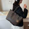 A woman holds a brown faux leather letter-print tote bag with gold hardware against a white background.