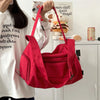 A bright red canvas crossbody travel tote bag is being held by a person against a white background.