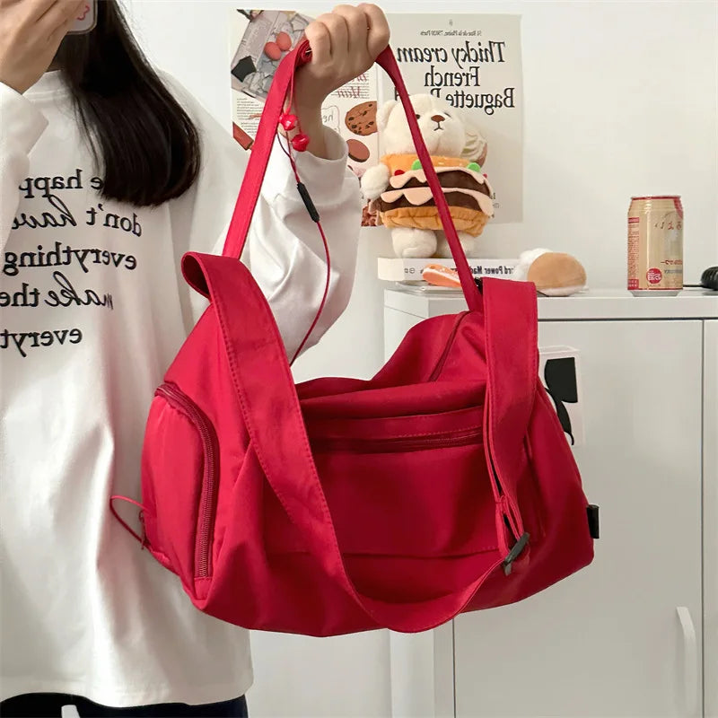 A bright red canvas crossbody travel tote bag is being held by a person against a white background.