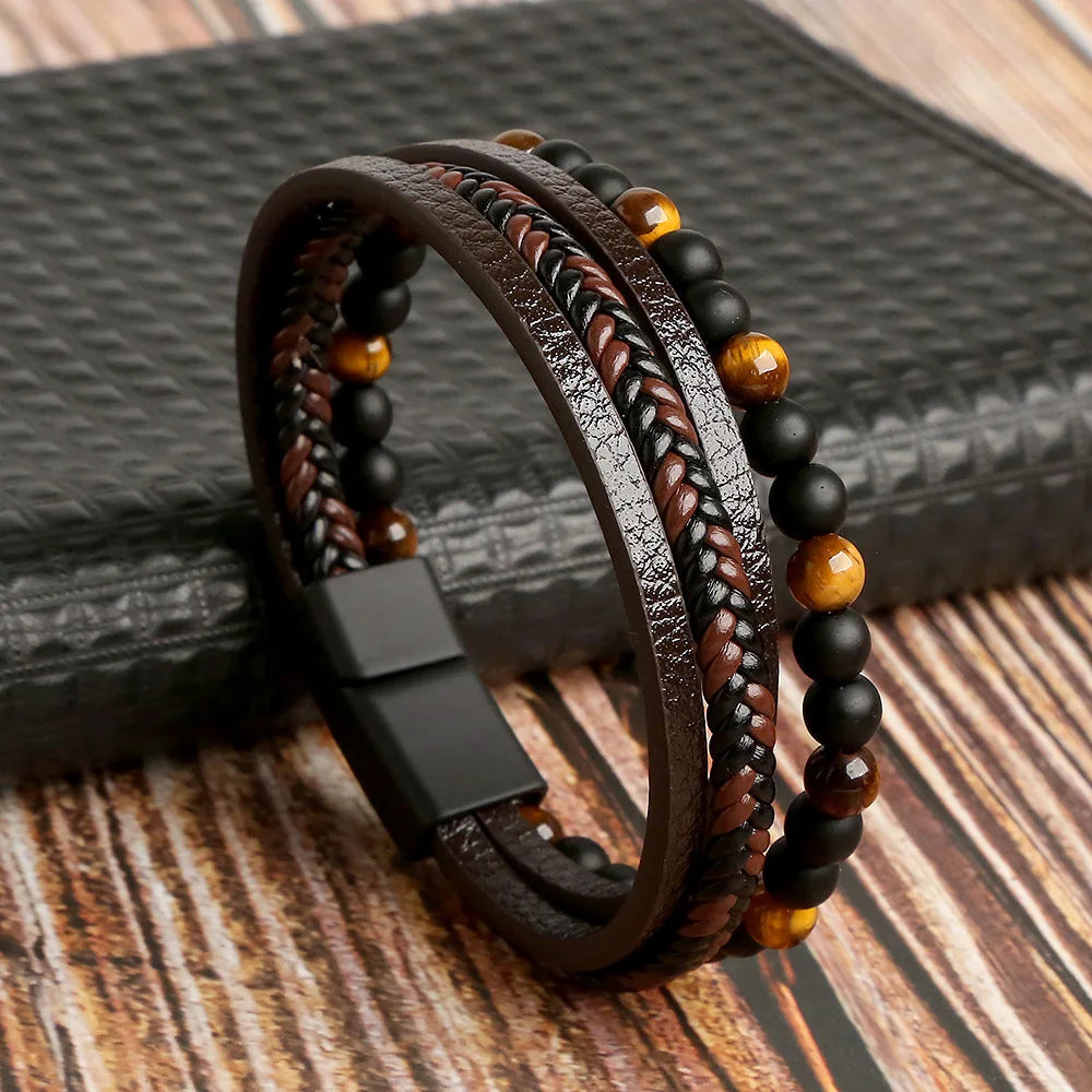A stack of multi-layer brown leather bracelets featuring tiger eye and black beads on a wooden surface.