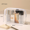 A clear PVC toiletry bag with a zipper closure holds several glass bottles and a brush.