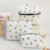 White quilted makeup bags with black trim and floral embroidery are displayed on a white surface.