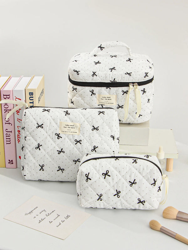 White quilted makeup bags with black trim and floral embroidery are displayed on a white surface.