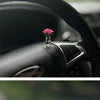 Eine kleine Glasvase mit einer rosa Rose liegt auf der Armaturenbrett und dem Lenkrad eines Autos.