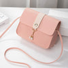 A light pink fashion square crossbody bag with a cream leather strap and gold-toned charm resting on a white surface.