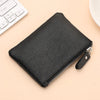 A black genuine leather mini zipper coin and card purse lying on a light beige surface next to a white computer keyboard.