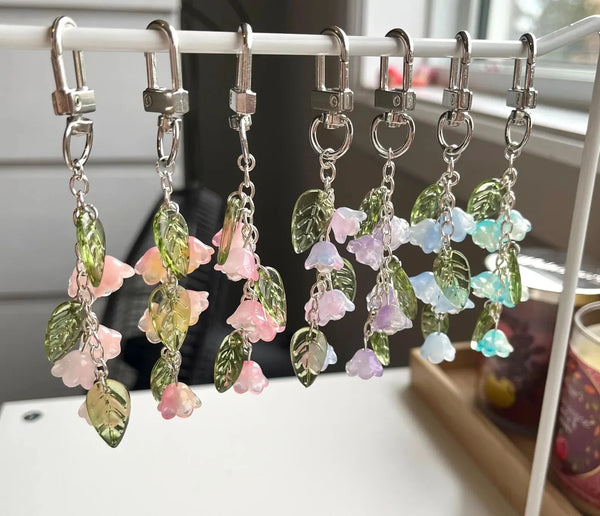Handmade Lily of the Valley flower keychains with various shades of green and pink foliage hanging on a white rack.