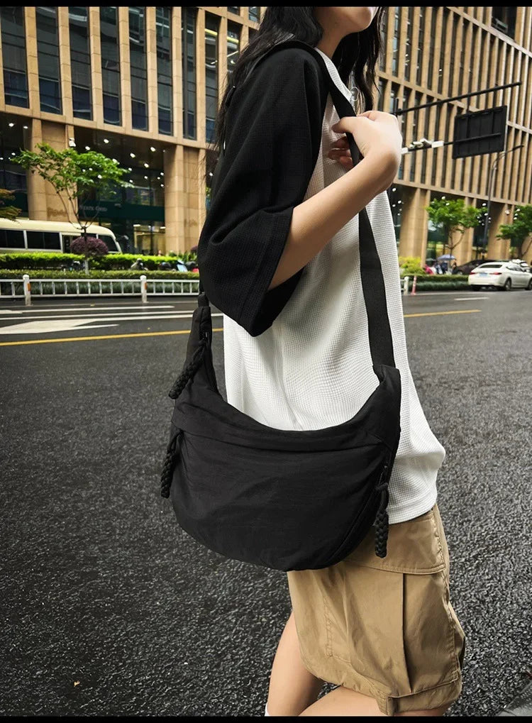 A woman wearing a black soft nylon crossbody shoulder bag while standing on an asphalt road.