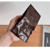 A hand holds a dark brown genuine leather bifold wallet for men.