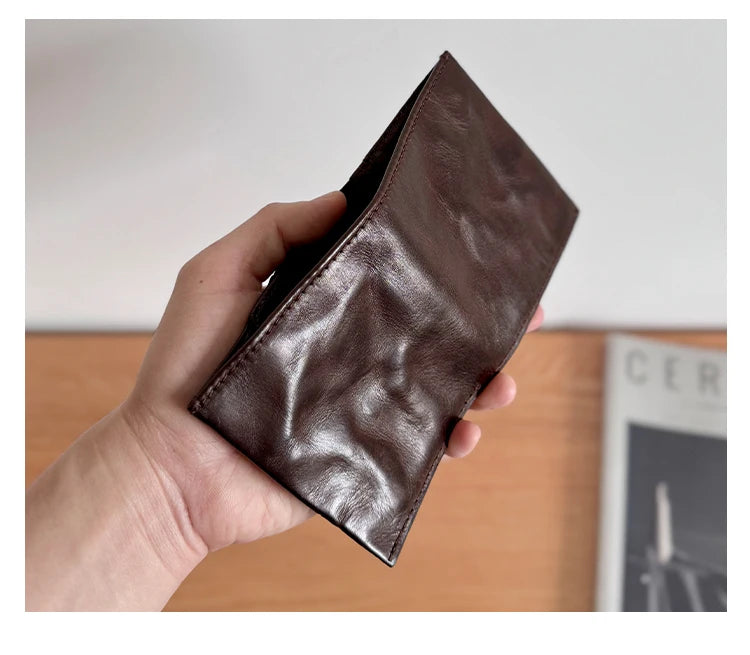 A hand holds a dark brown genuine leather bifold wallet for men.