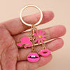 A gold-colored enamel heart keychain featuring a pink flower and a pink lips charm, held in a hand.