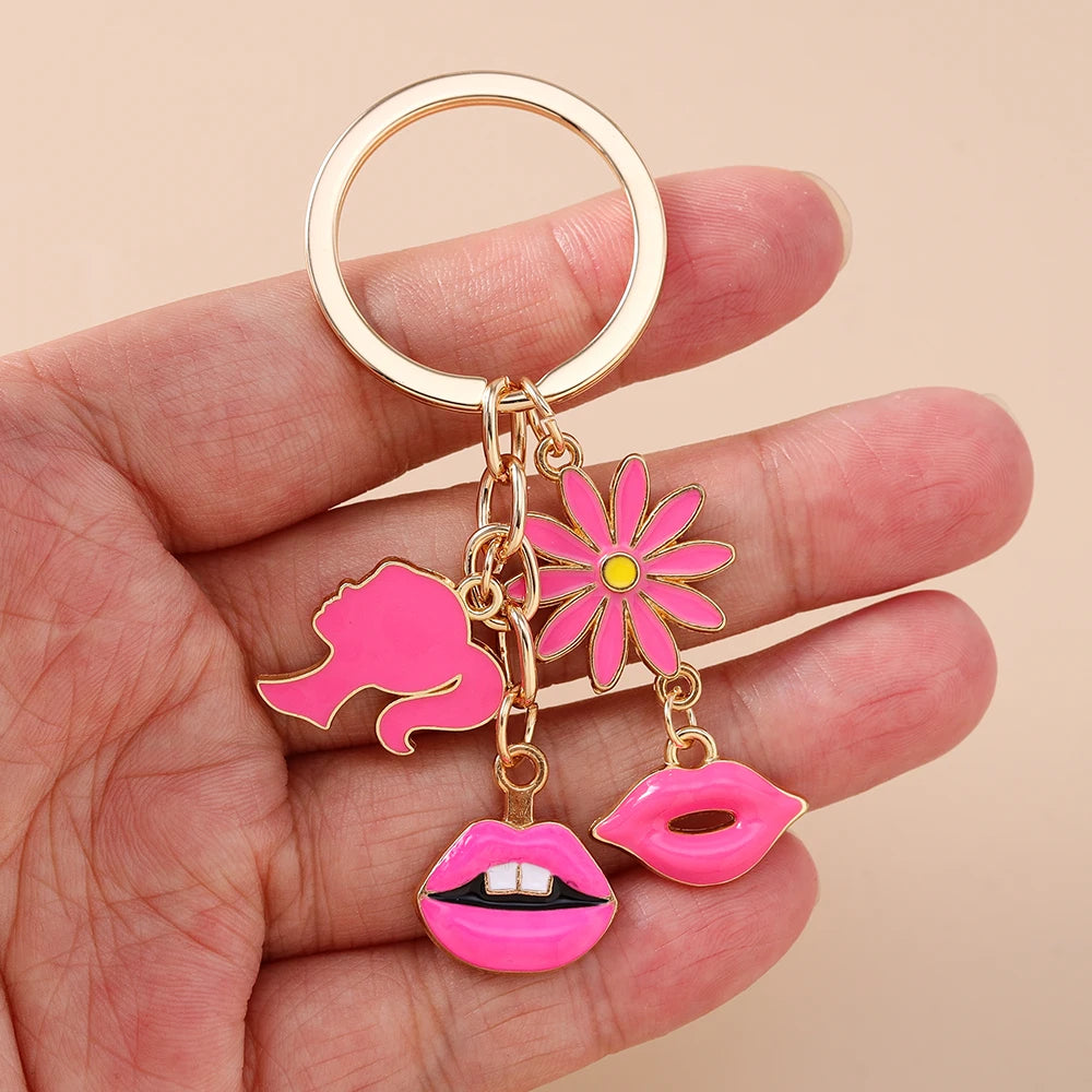 A gold-colored enamel heart keychain featuring a pink flower and a pink lips charm, held in a hand.