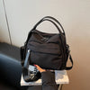A black multi-pocket nylon crossbody bag with a top handle is displayed on a white surface.
