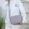 Eine Frau hält eine helllila Nylon-Crossbody-Tasche vor einem weiß gestreiften Langarmshirt.
