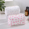 Bolsa acolchada blanca para maquillaje con estampado de lazo rosa en fondo blanco.