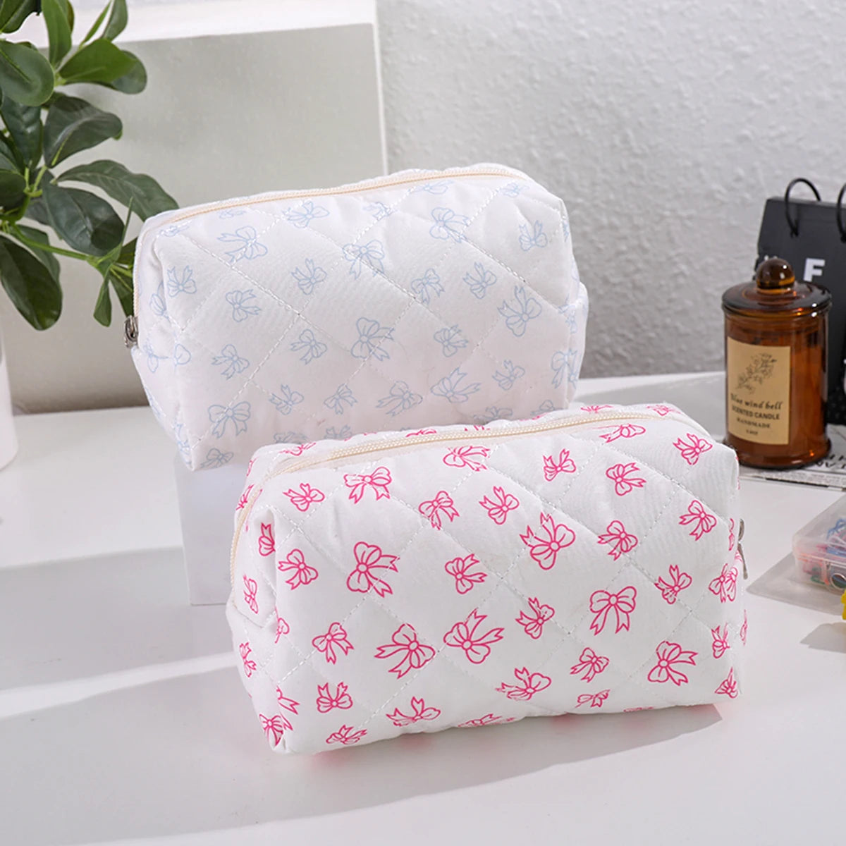 Bolsa acolchada blanca para maquillaje con estampado de lazo rosa en fondo blanco.