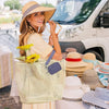 A woman wearing a straw hat holds a light green mesh coin purse and is standing next to a white van.