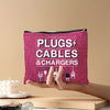 A hand holds a magenta zippered pouch labeled PLUGS CABLES & CHARGERS against a beige background.