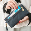 A hand is opening a dark blue retro long wallet with a gold zipper and a card visible inside.