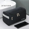 A black durable hanging leather toiletry bag next to a smartphone and a white ceramic sink.