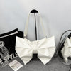 A white pleated bow crossbody tote bag displayed against a gray background.