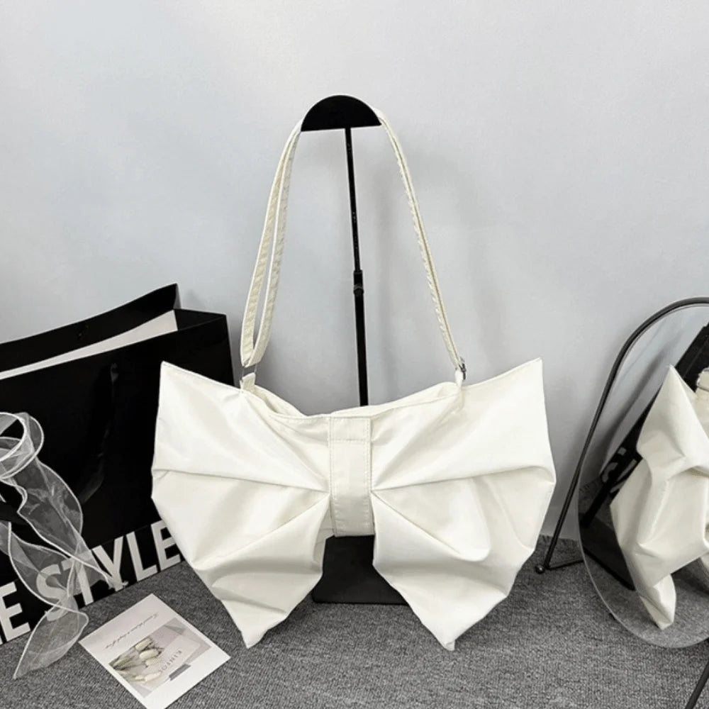 A white pleated bow crossbody tote bag displayed against a gray background.