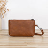 A brown retro PU leather zipper wrist bag resting on a light wooden surface.