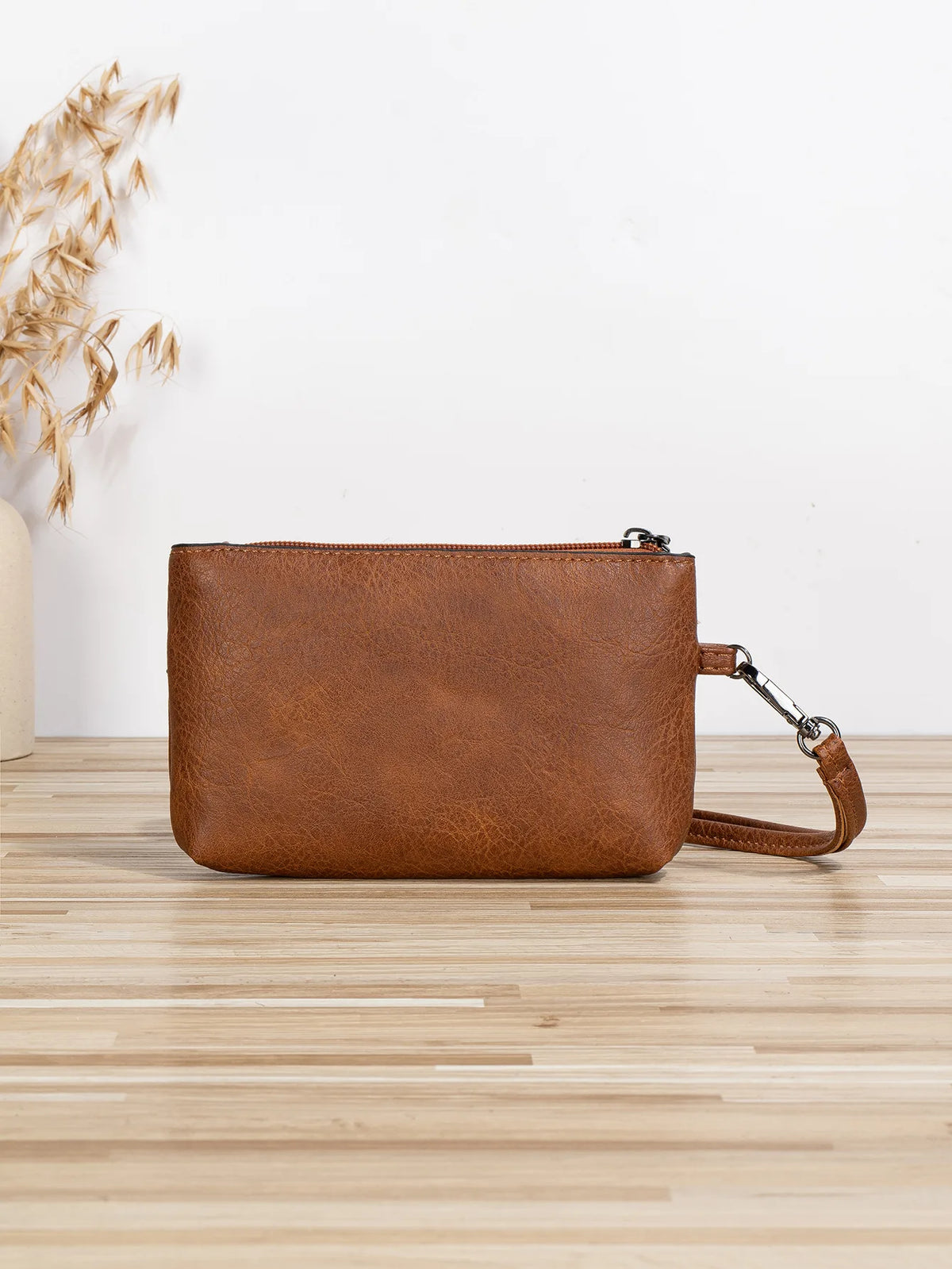 A brown retro PU leather zipper wrist bag resting on a light wooden surface.