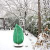 A green plant protection cover with a zipper and drawstring is displayed outdoors in a snowy garden setting.