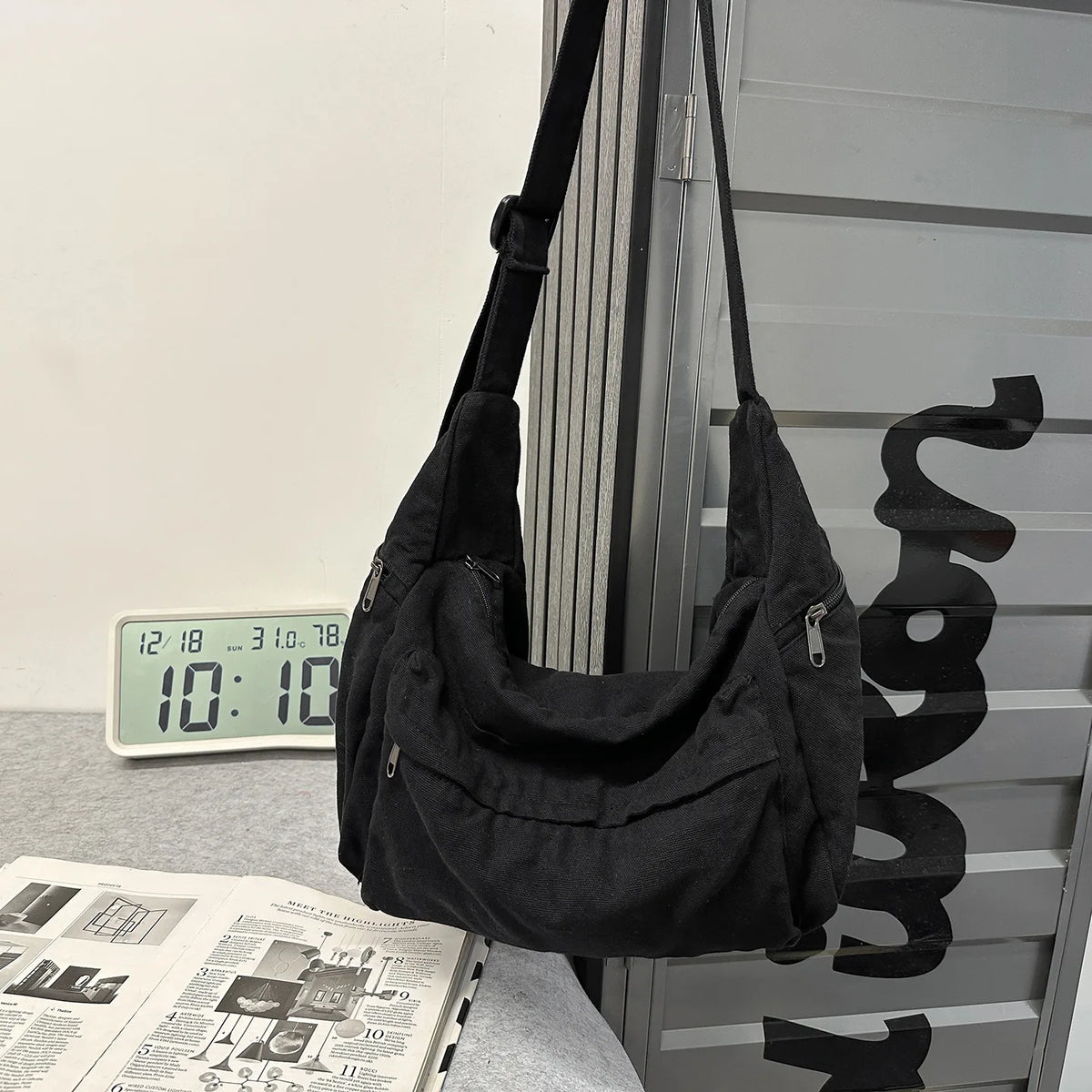 A black large capacity cotton canvas shoulder crossbody bag hanging against a gray vertical surface.