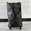 A black foldable lightweight shopping cart with wheels standing on a gray floor.