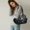 Eine Frau in grauem Rollkragenpullover und Jeans hält eine schwarze Vintage-Handtasche aus weichem Kunstleder.